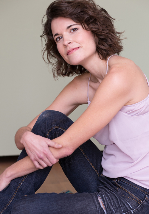 A white woman wiht shoulder-length brown hair wearing jeans and a pale pink blouse