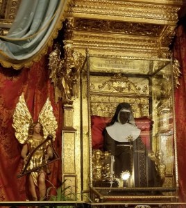 A glass case holding a Nun outfit, surrounded by ornate gold