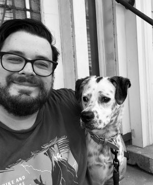 Black and white photograph of a man smiling at the camera beside his dog